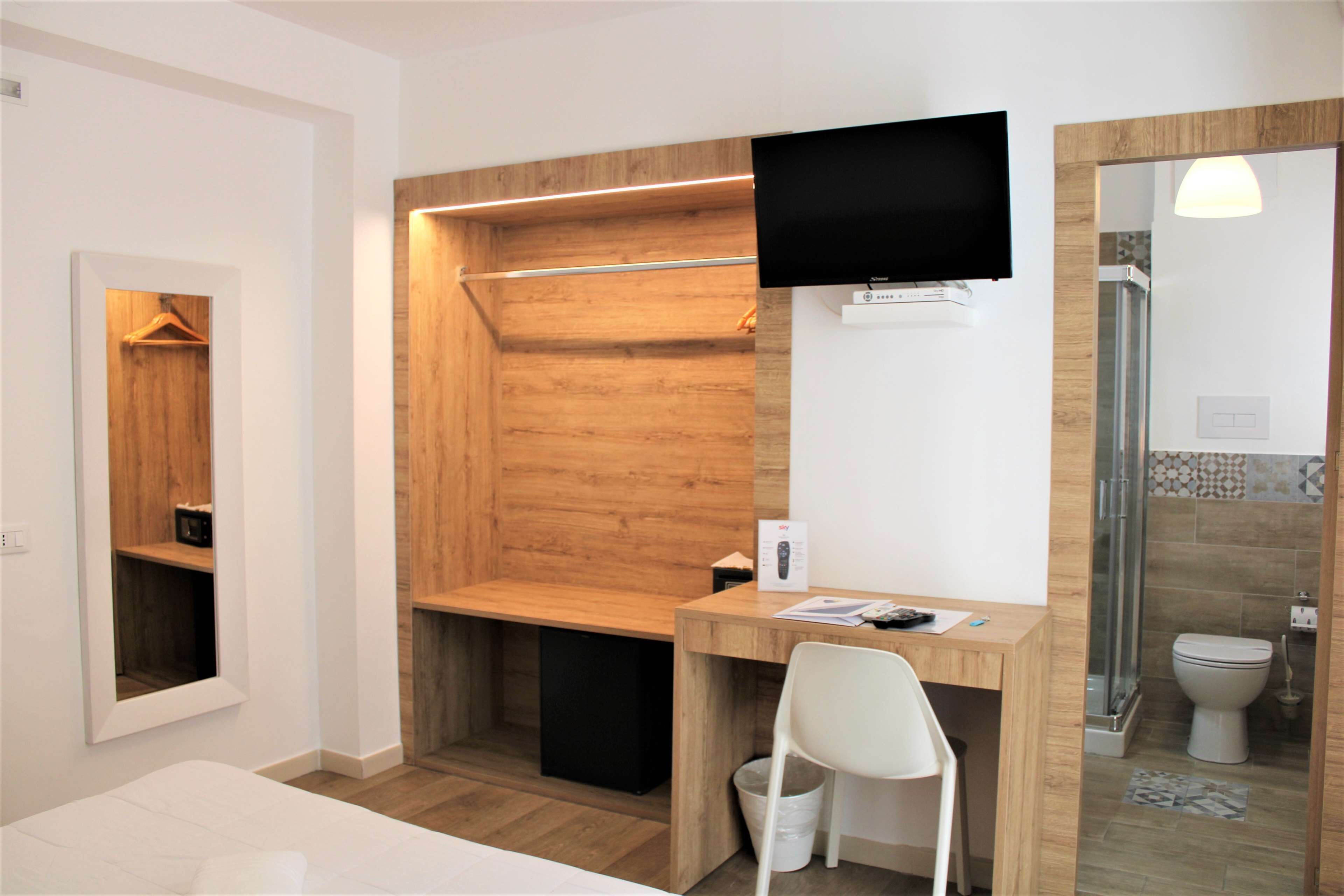 A modern bathroom with a wooden shower enclosure, a mounted TV, and a small desk with a chair.