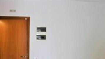 Una stanza con una porta in legno, un letto con materasso bianco e coperta viola, e una piccola insegna fissata al muro.
