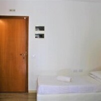 Una stanza con una porta in legno, un letto con materasso bianco e coperta viola, e una piccola insegna fissata al muro.