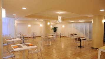 Un'ampia sala conferenze con tavoli e sedie, un lampadario e grandi finestre con tende.