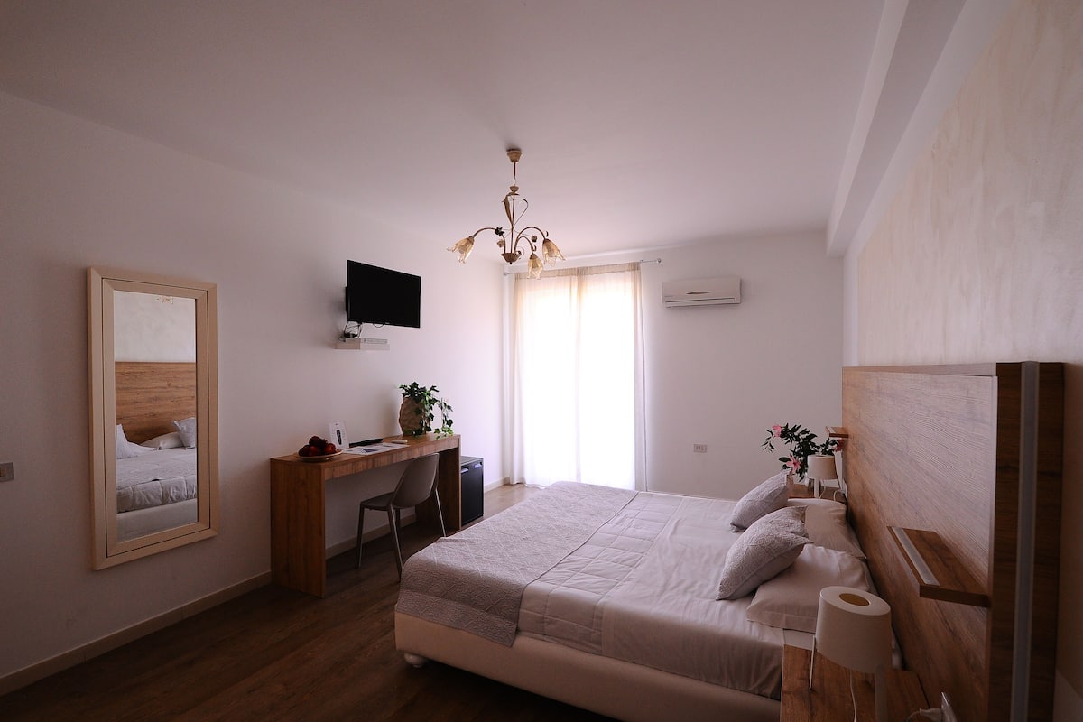 A bedroom with a bed, a desk, a chair, a television, and a window with curtains.
