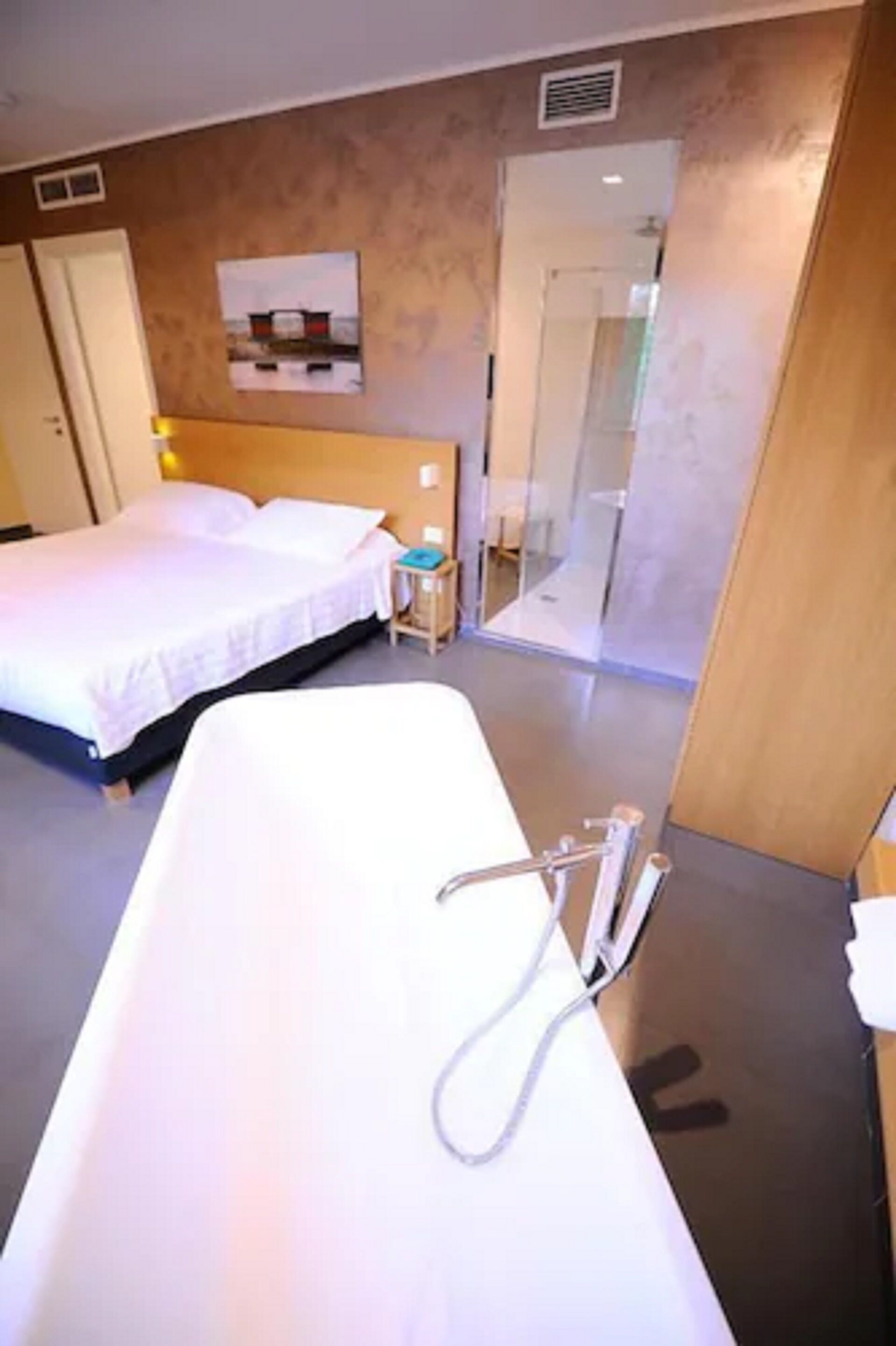 Una camera d'albergo con un letto, un comodino, uno specchio e un angolo doccia.