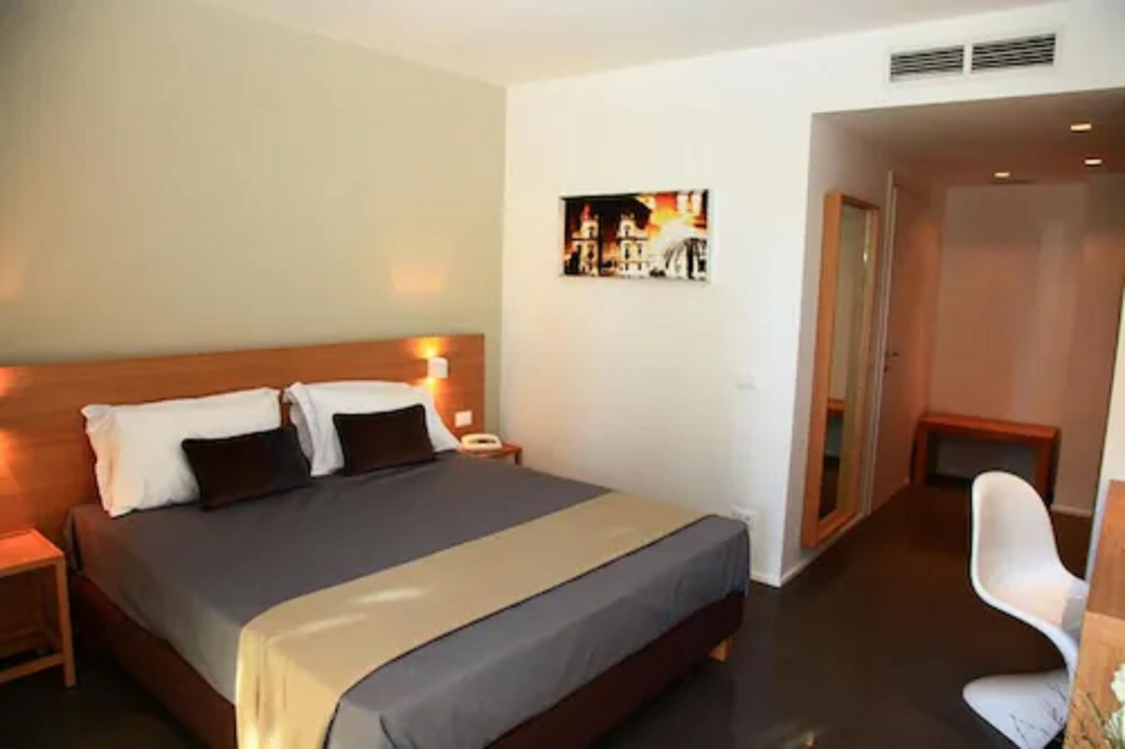 Een hotelkamer met een groot bed, nachtkastjes, een stoel en een schilderij aan de muur.