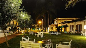 An outdoor seating area with tables and chairs, surrounded by greenery and illuminated by ambient lighting. - Casena Dei Colli, Sure Hotel Collection by Best Western (Palermo)