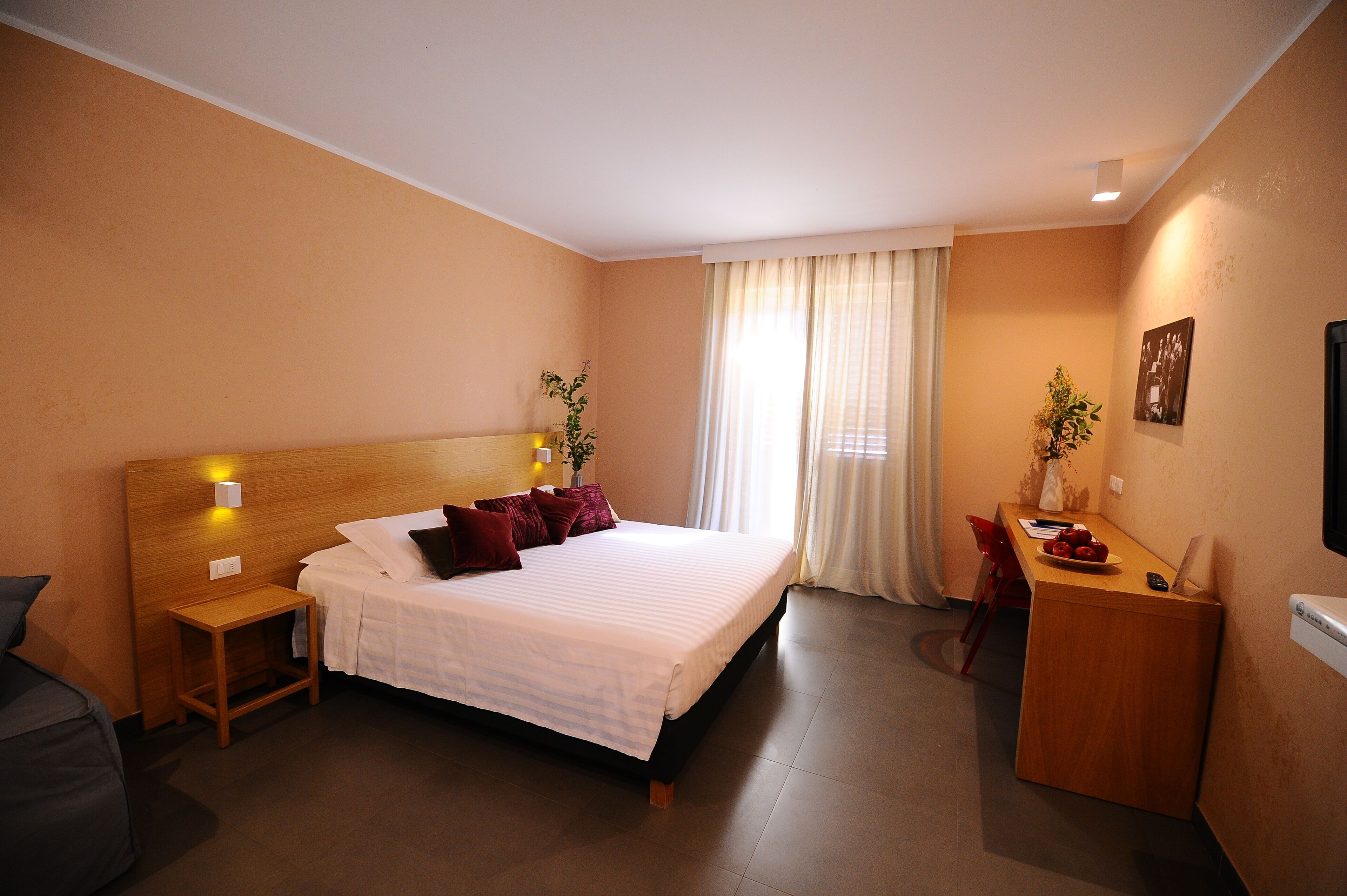 Habitación de hotel con cama, mesita de noche, escritorio, silla y ventana con cortinas.