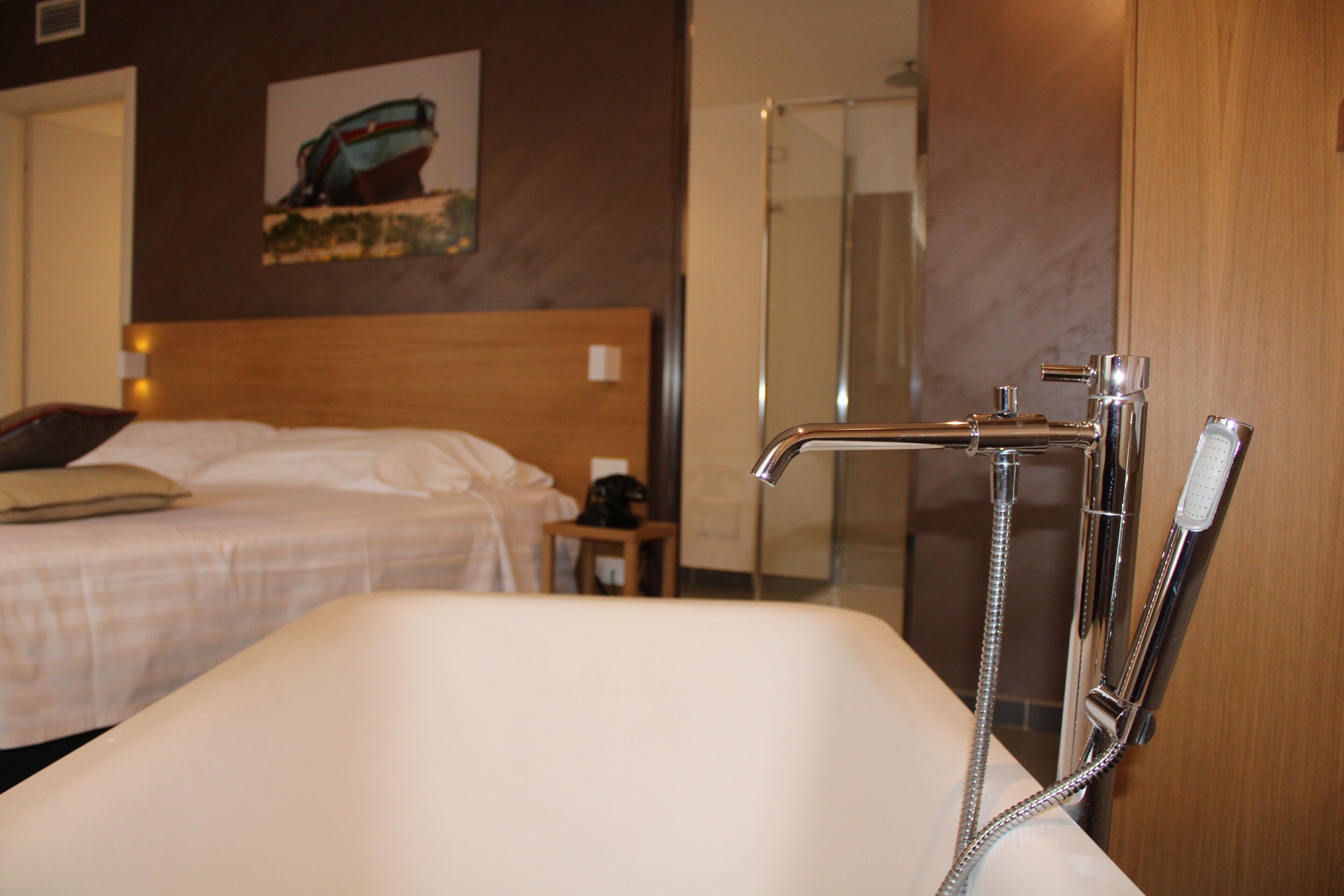 A hotel bathroom with a bathtub, a shower, and a bed with a headboard.