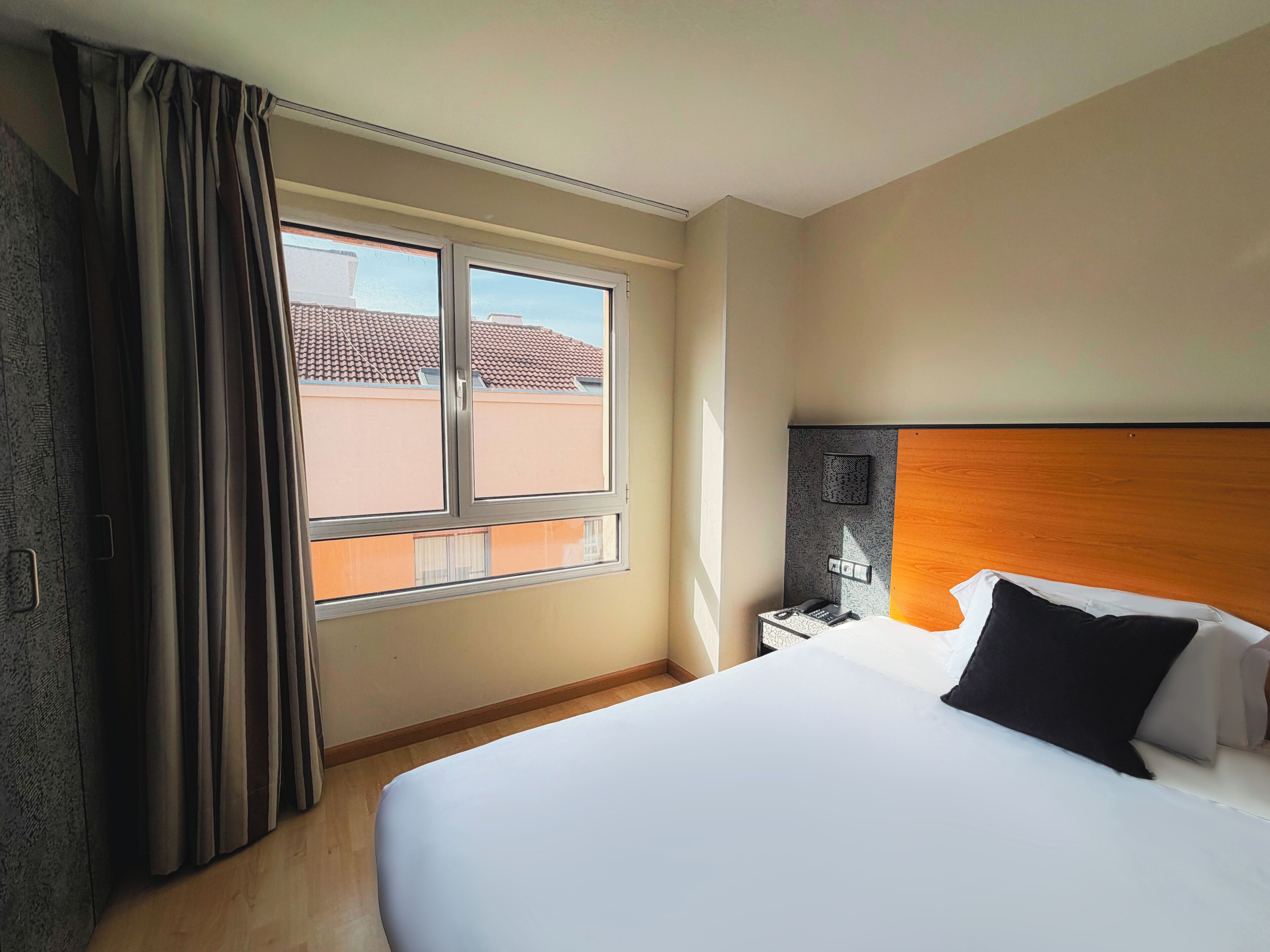 Een hotelkamer met een groot bed, een nachtkastje, een lamp en een raam met gordijnen.