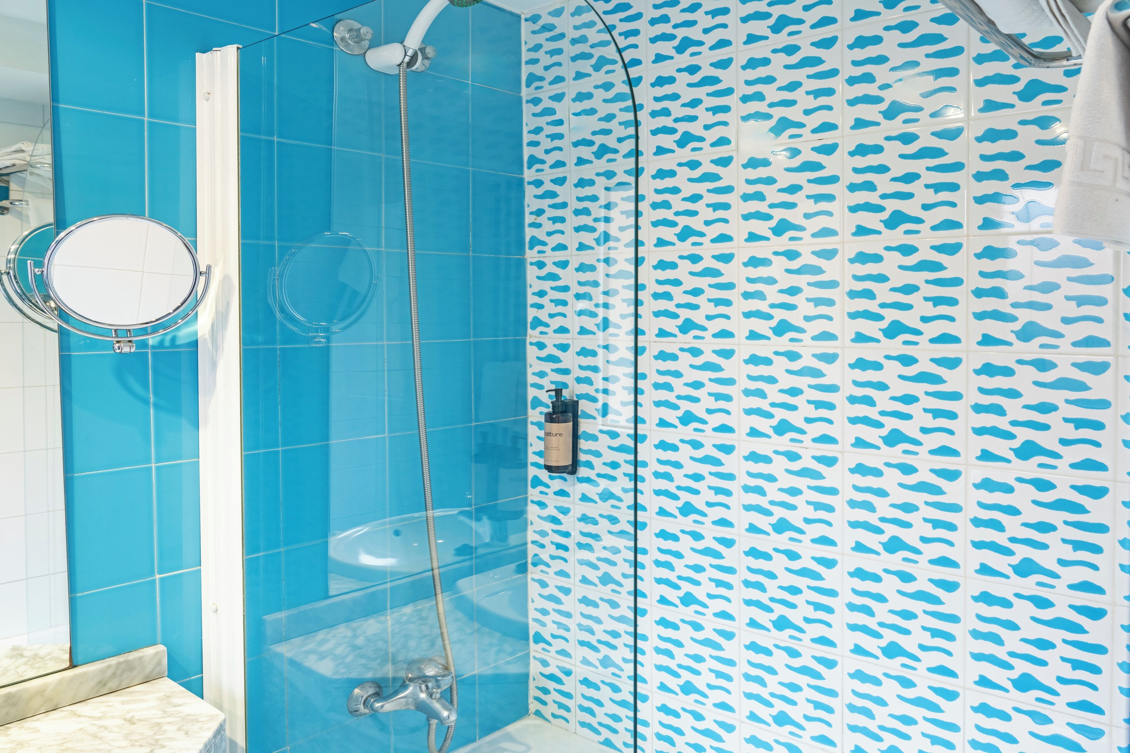 Un baño con azulejos azules, una ducha y un revestimiento de pared estampado.