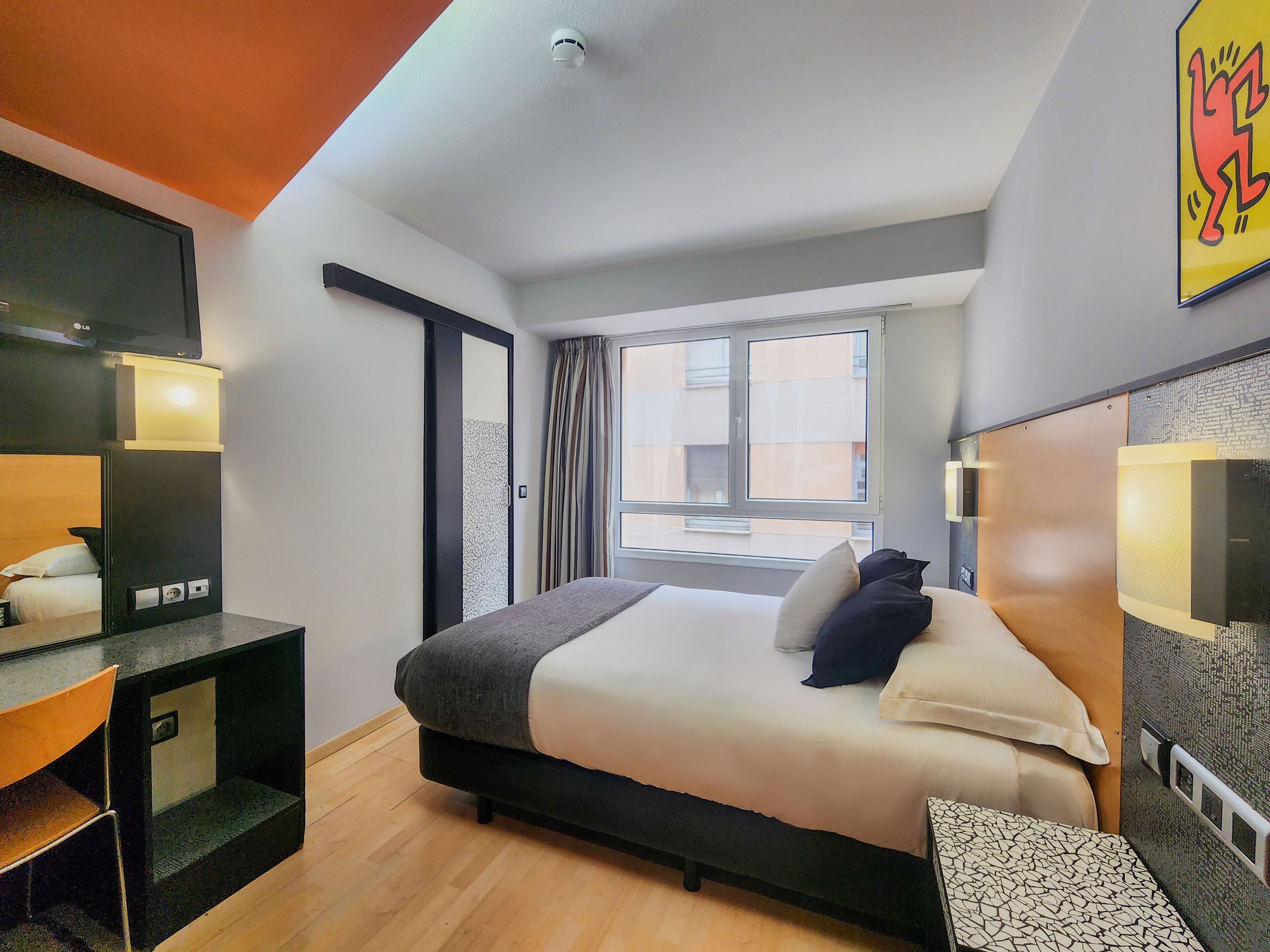 A modern hotel room with a bed, a desk, a chair, a window, and a bathroom.