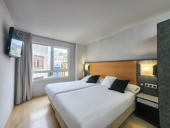 Une chambre d’hôtel avec deux lits, un téléviseur fixé au mur et une fenêtre avec des rideaux.