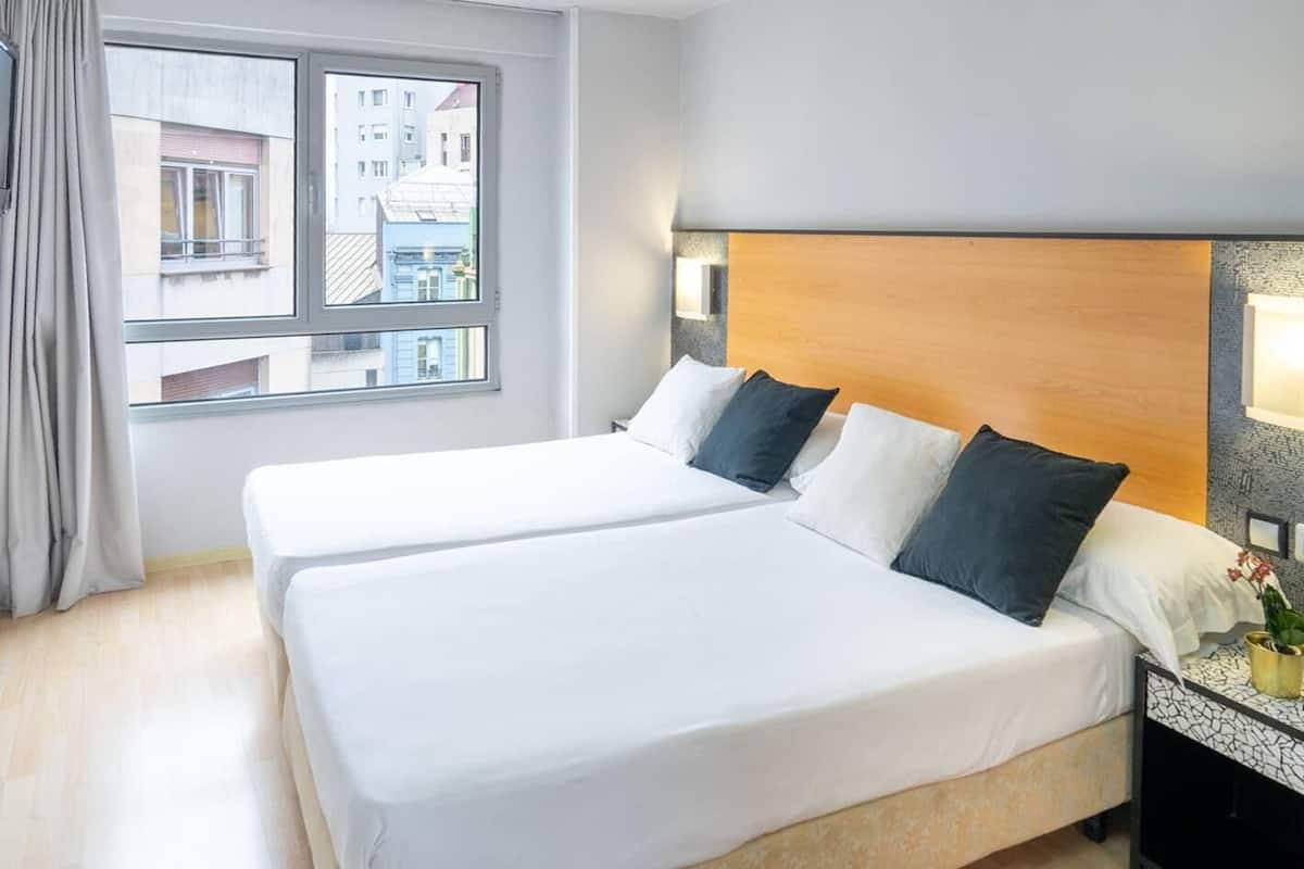 Une chambre d’hôtel avec deux lits, une grande fenêtre et une vue sur les bâtiments environnants.
