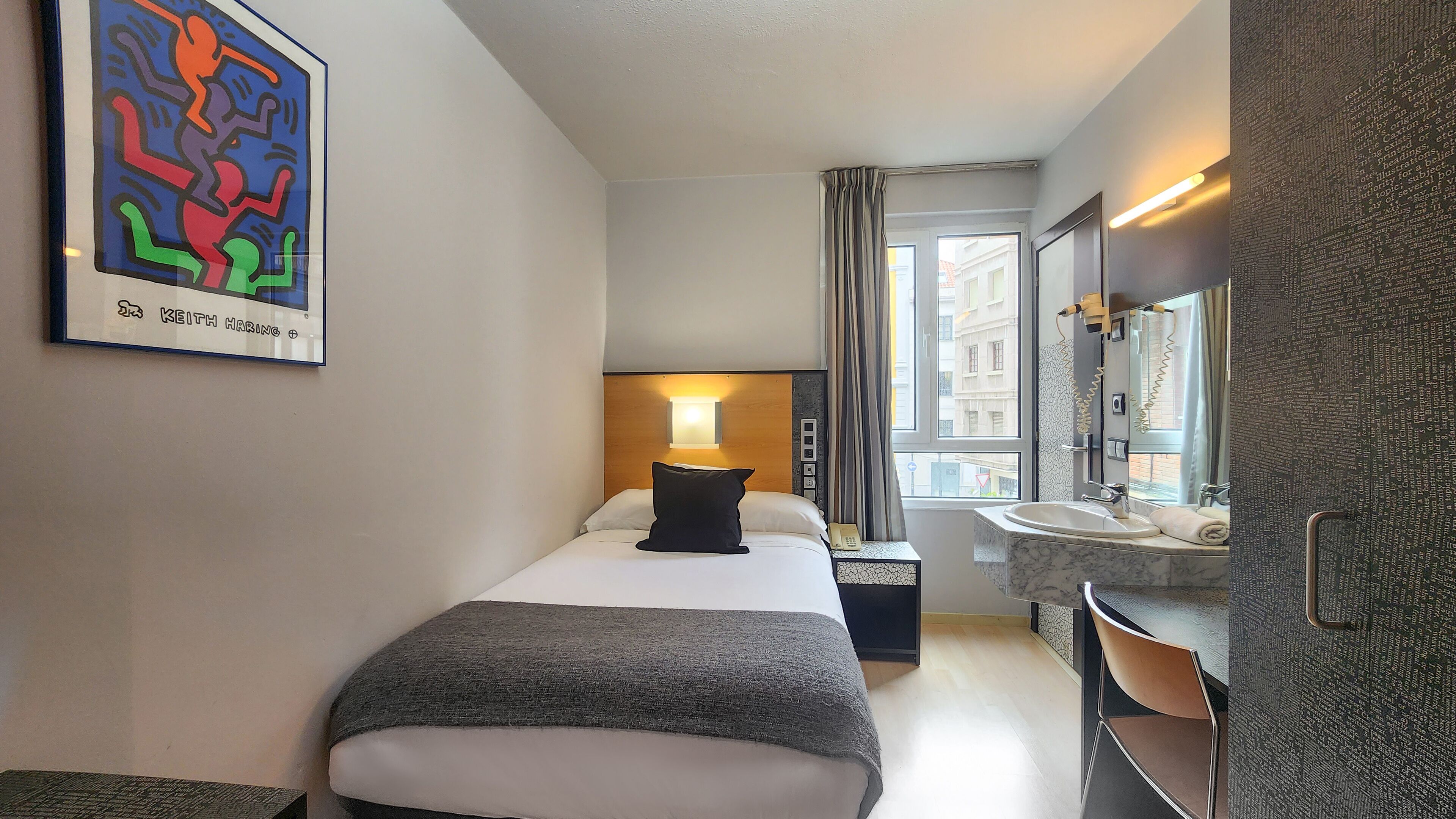 A hotel room with a bed, bedside table, lamp, and a bathroom with a sink and mirror.