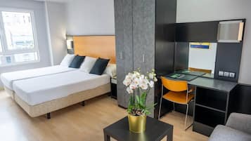 A modern hotel room with a double bed, a desk with a chair, a large wardrobe, and a potted orchid.