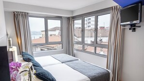 Une chambre à coucher avec un lit, une télévision et de grandes fenêtres avec des rideaux.