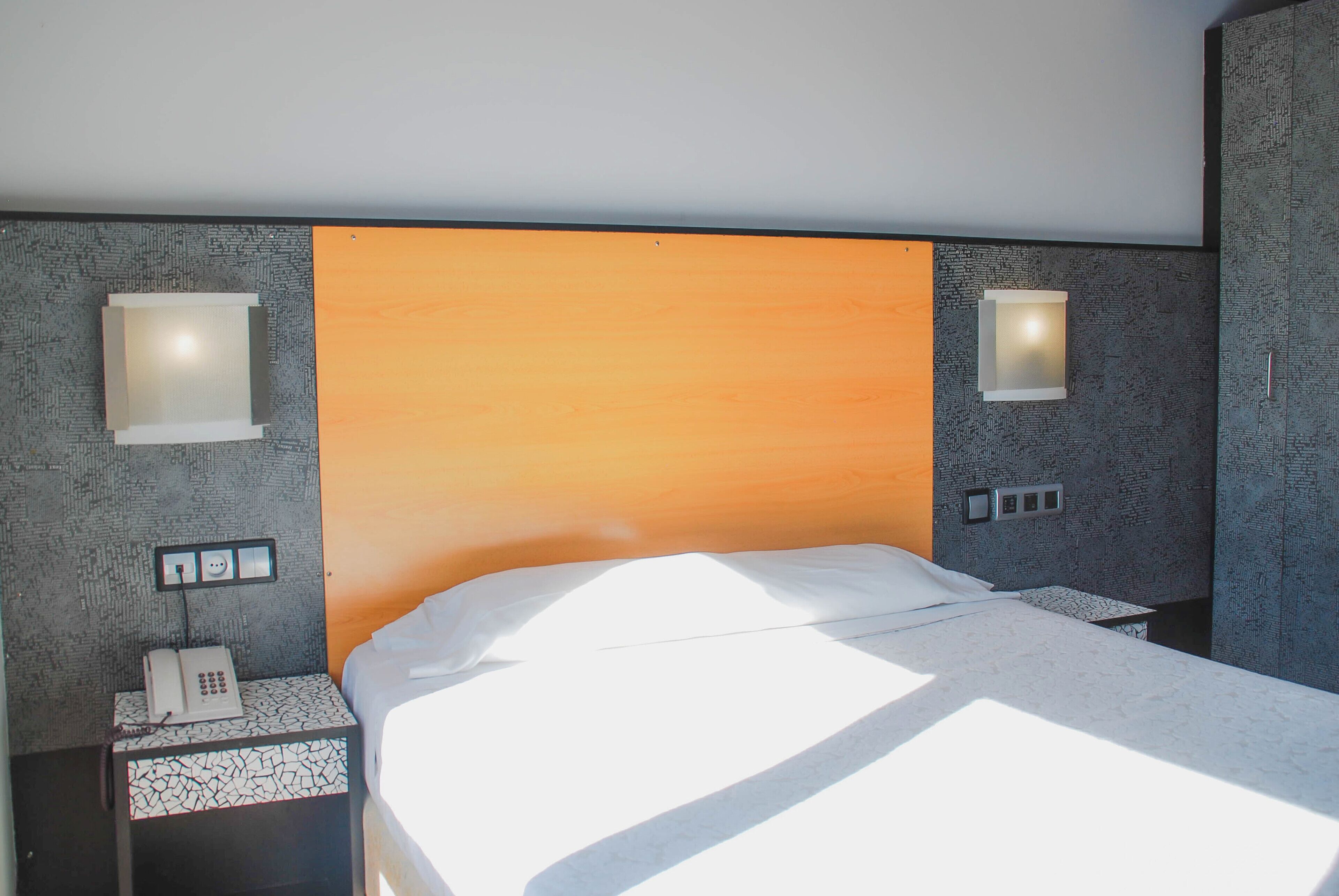 A hotel room with a bed, a nightstand with a phone, and two wall-mounted light fixtures.