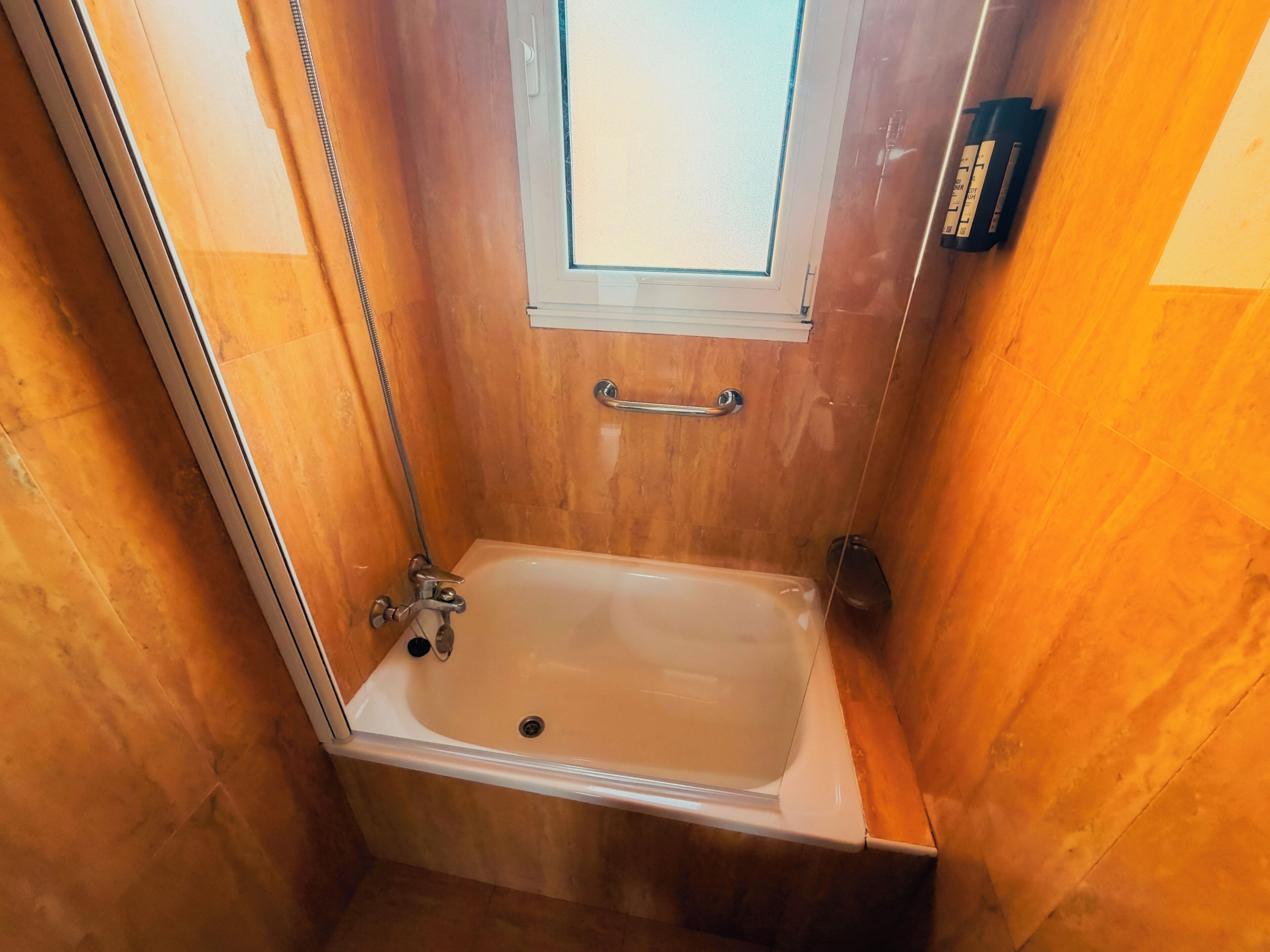 A small, wooden-finished bathroom with a bathtub, a window, and a towel rack.