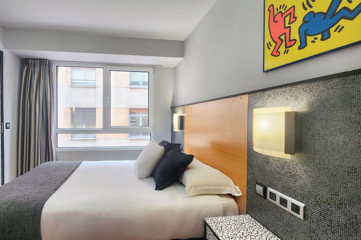 Ein Hotelzimmer mit einem großen Bett, einem Nachttisch, einem Fenster mit Vorhängen und einer Wand mit einer Zierleiste.