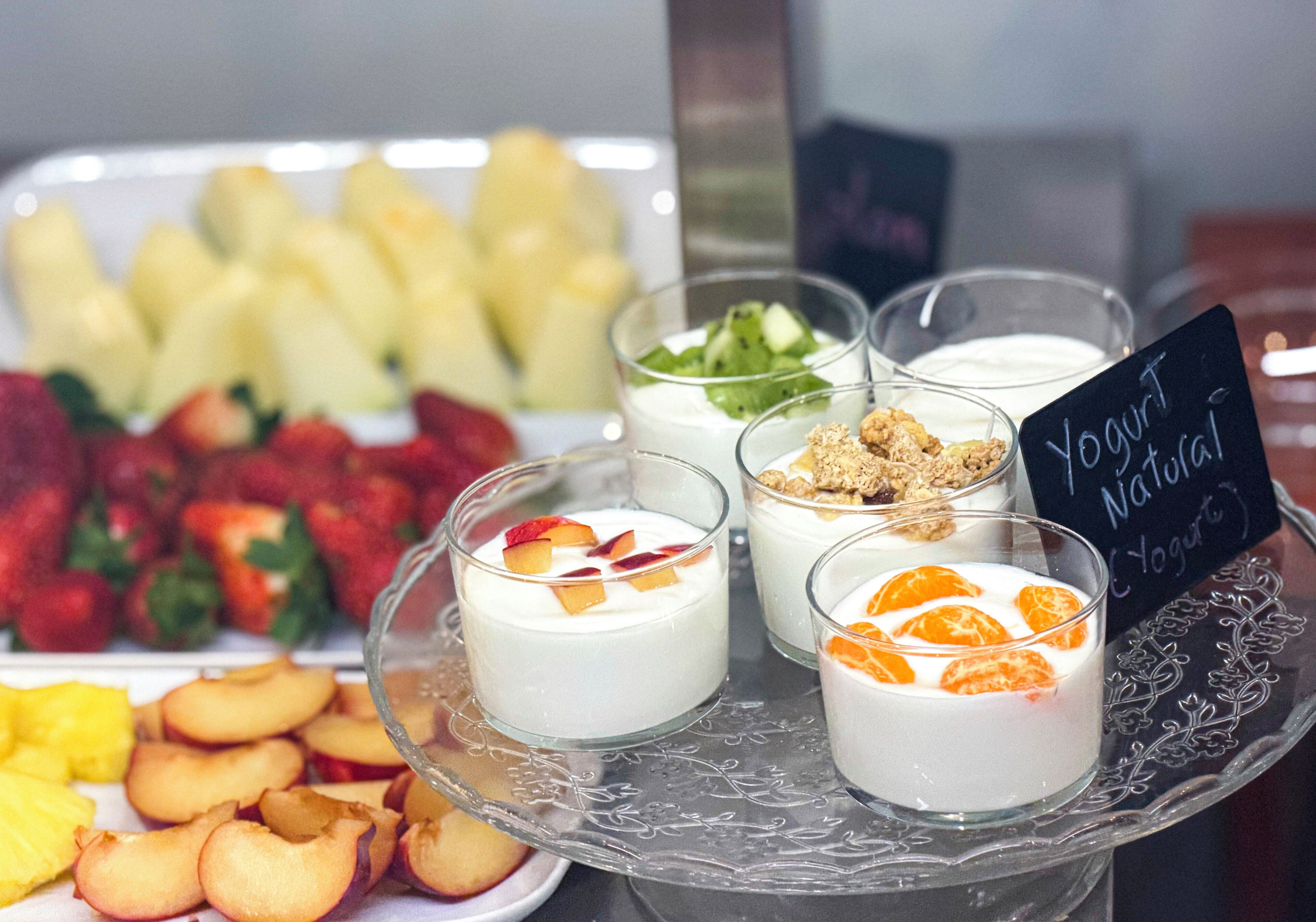 Variedad de vasos de parfait de yogur con frutas y granola, junto con frutas frescas en una bandeja.