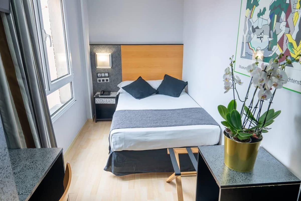 Une chambre d’hôtel avec un lit, une table de chevet, une commode et une fenêtre.