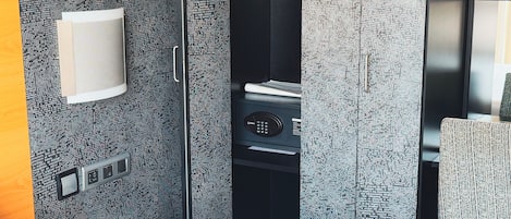 A modern hotel room with a bed, a desk, a chair, a small table, a wall-mounted control panel, and a large window.