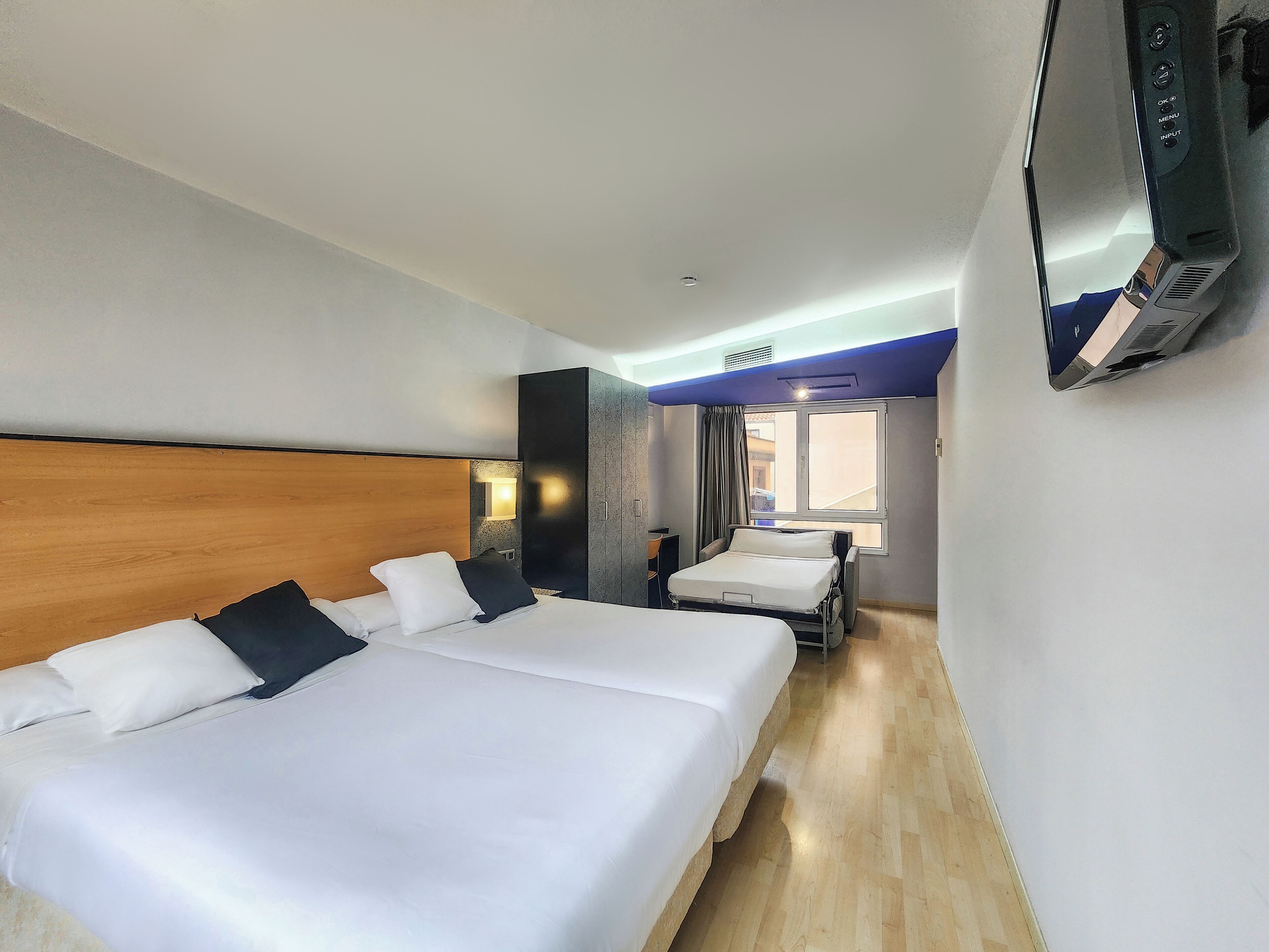 A hotel room with two beds, a TV, a window with curtains, and a wooden headboard.