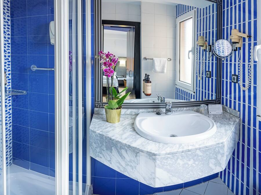 Une salle de bain avec des carreaux bleus à motifs, un lavabo blanc, un miroir et une orchidée en pot.