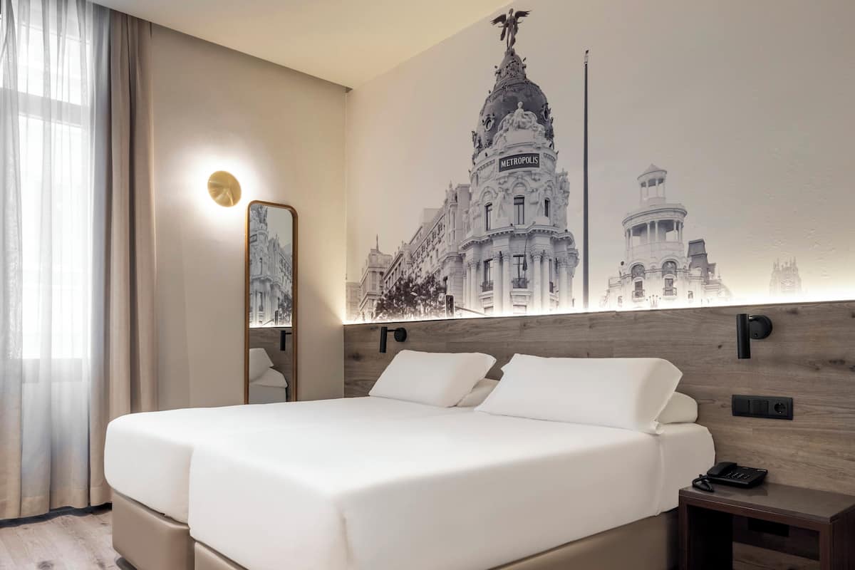 Une chambre d’hôtel avec un grand lit, une table de chevet, un miroir et une lampe fixée au mur.