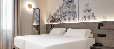 Habitación de hotel con una cama grande, una mesita de noche, un espejo y una lámpara de pared.