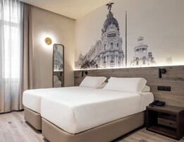 A hotel room with a large bed, a nightstand, a mirror, and a wall-mounted light.