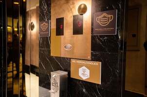 An elevator interior with a hand sanitizer dispenser, a face mask sign, and a sign indicating the elevator is empty.