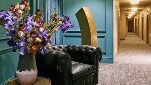 A hallway with teal walls, a black leather chair, and a vase of purple flowers. - Hotel Regente (Madrid)