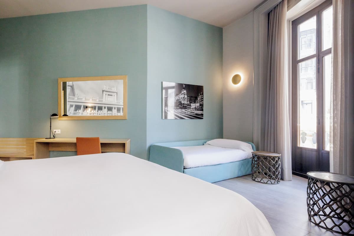 Une chambre d’hôtel avec un grand lit, un bureau, une chaise, une petite table et deux tableaux encadrés au mur.
