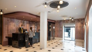A hotel lobby with a reception desk, a large pillar, a marble wall, and a check-in counter. - Hotel Regente (Madrid)