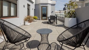 A rooftop terrace with two black wire mesh chairs, a small round table, and potted plants. - Hotel Regente (Madrid)