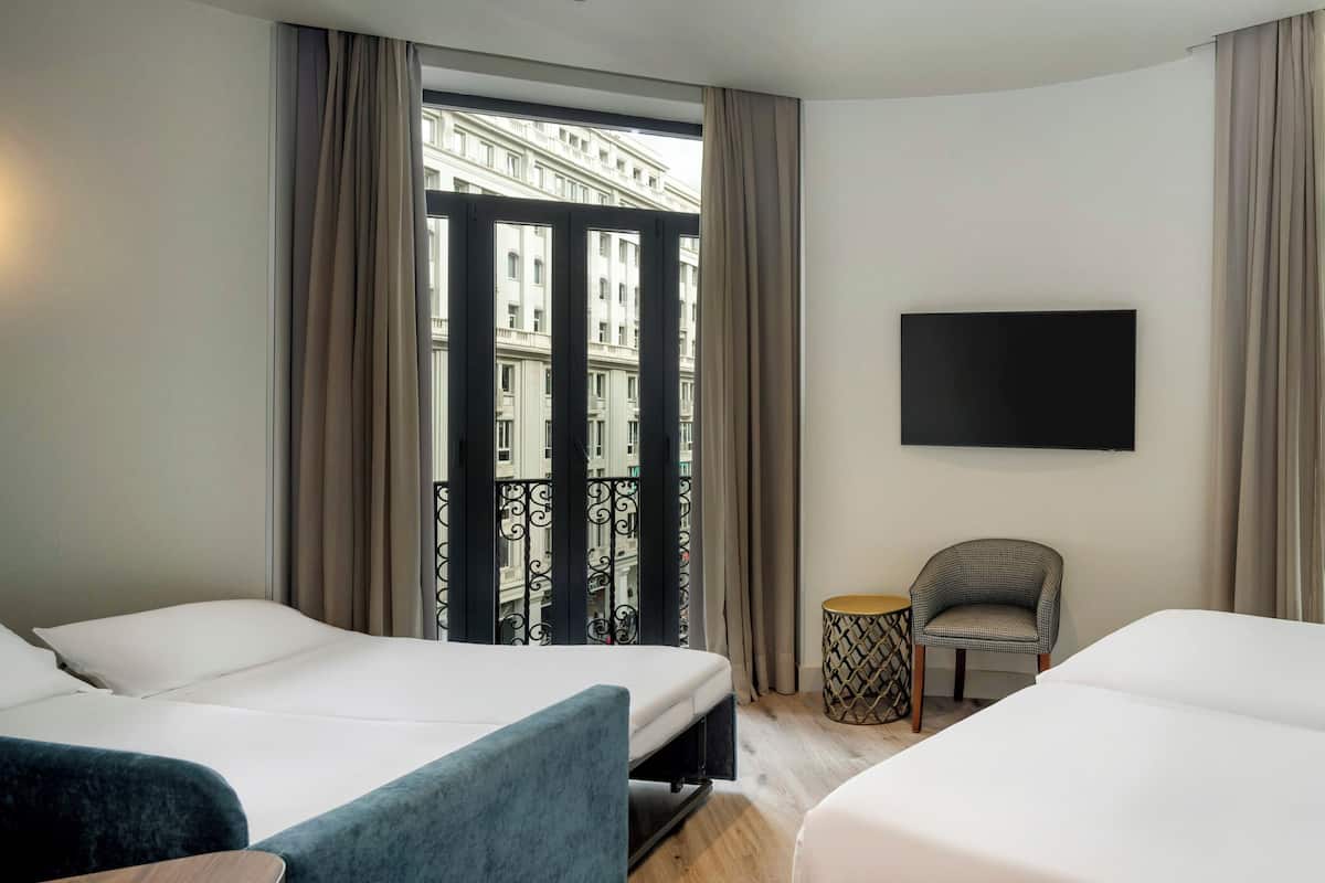 Une chambre d’hôtel avec deux lits, une télévision, une chaise et une vue sur les immeubles.