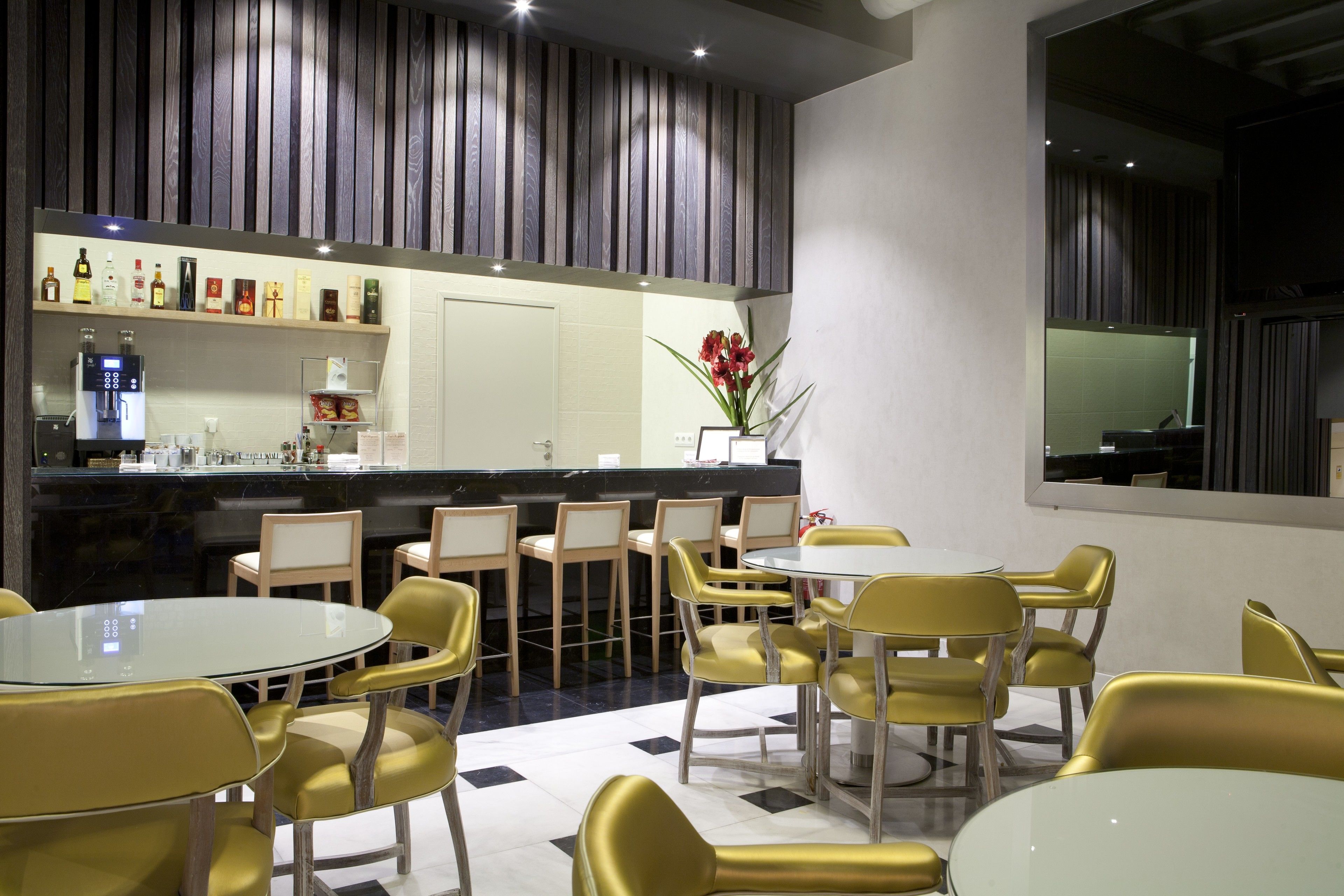 A modern dining area with round tables and yellow chairs, a bar with a variety of liquor bottles, and a decorative plant.