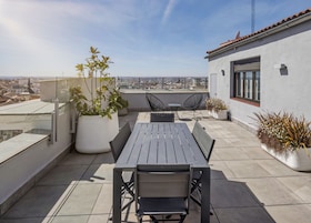A rooftop terrace with a table and chairs, potted plants, and a city view.