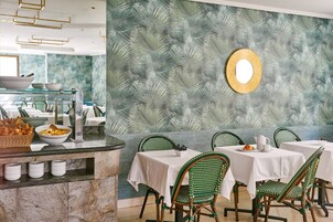 A dining area with a tropical leaf-patterned wall, green wicker chairs, and a buffet counter with food items.