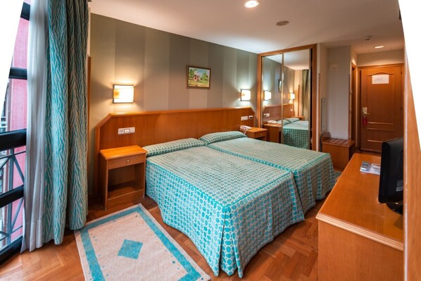 A hotel room with two beds, a desk, a chair, a TV, and a window with curtains.