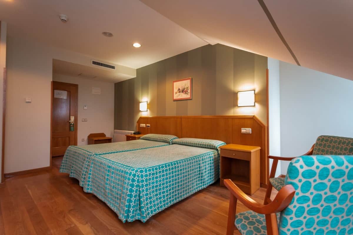 A hotel room with a wooden bed, two bedside tables, a chair, and a wall-mounted lamp.