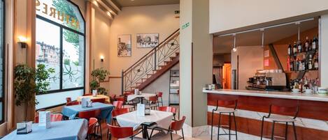 A restaurant with tables and chairs, a bar area, and a staircase leading to an upper level.
