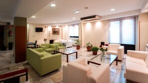 A modern hotel lobby with seating areas, a reception desk, and a large window providing natural light. - Hotel Astures (Oviedo)
