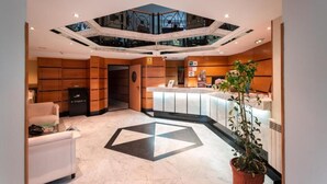 A hotel lobby with a reception desk, a seating area, and a geometric floor design. - Hotel Astures (Oviedo)