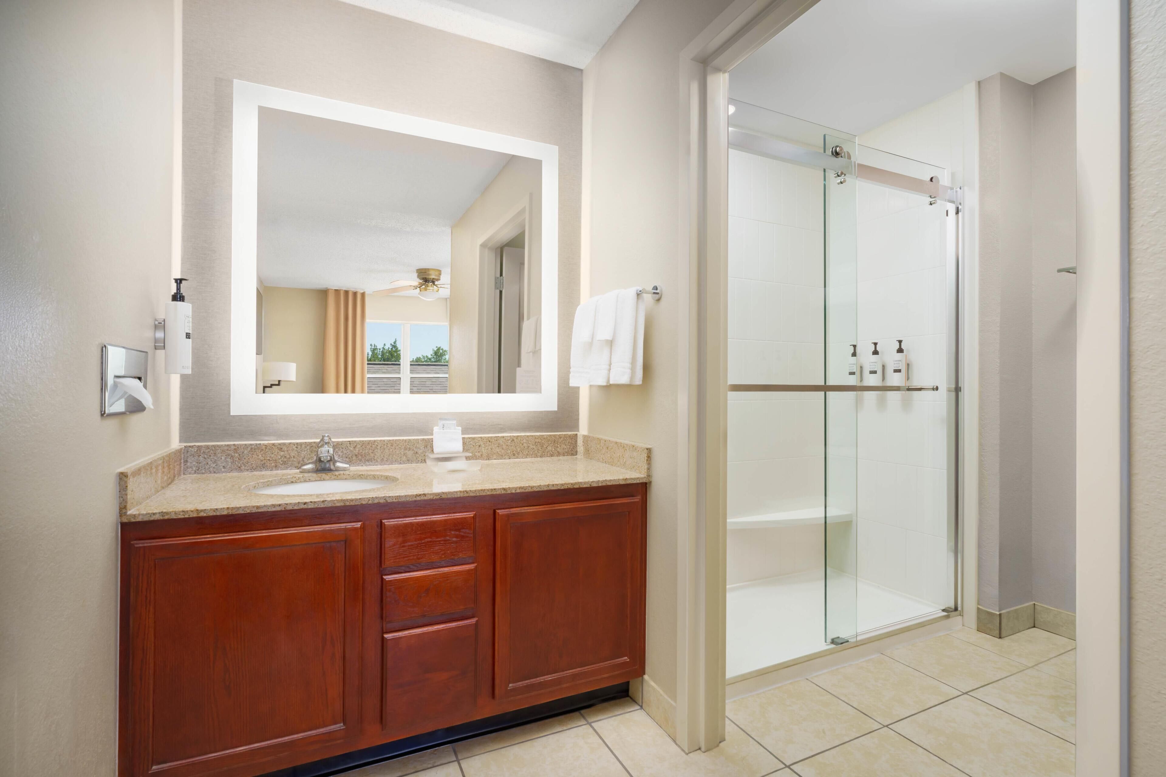 A modern bathroom with a large mirror, a sink, wooden vanity, and a glass-enclosed shower.