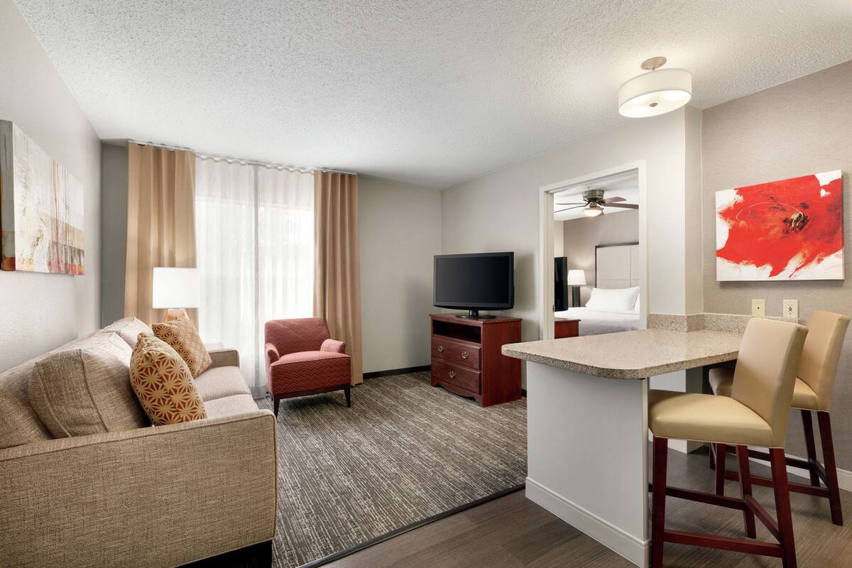 Hotelkamer met een zithoek, een televisie, een kleine kitchenette en een plafondventilator.