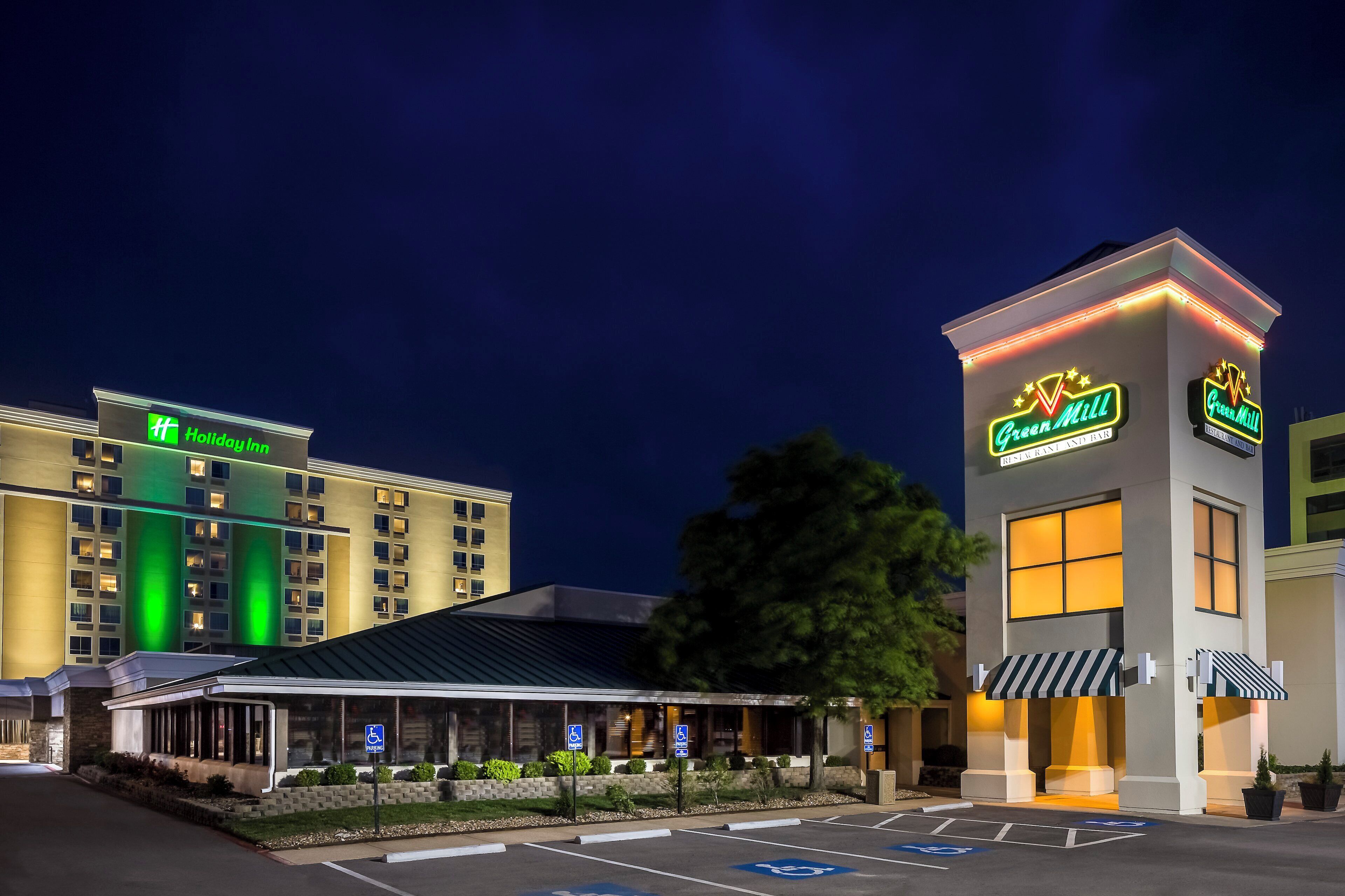 A hotel with a green-lit sign, a restaurant named Green Mill, and a parking area with handicapped accessibility.