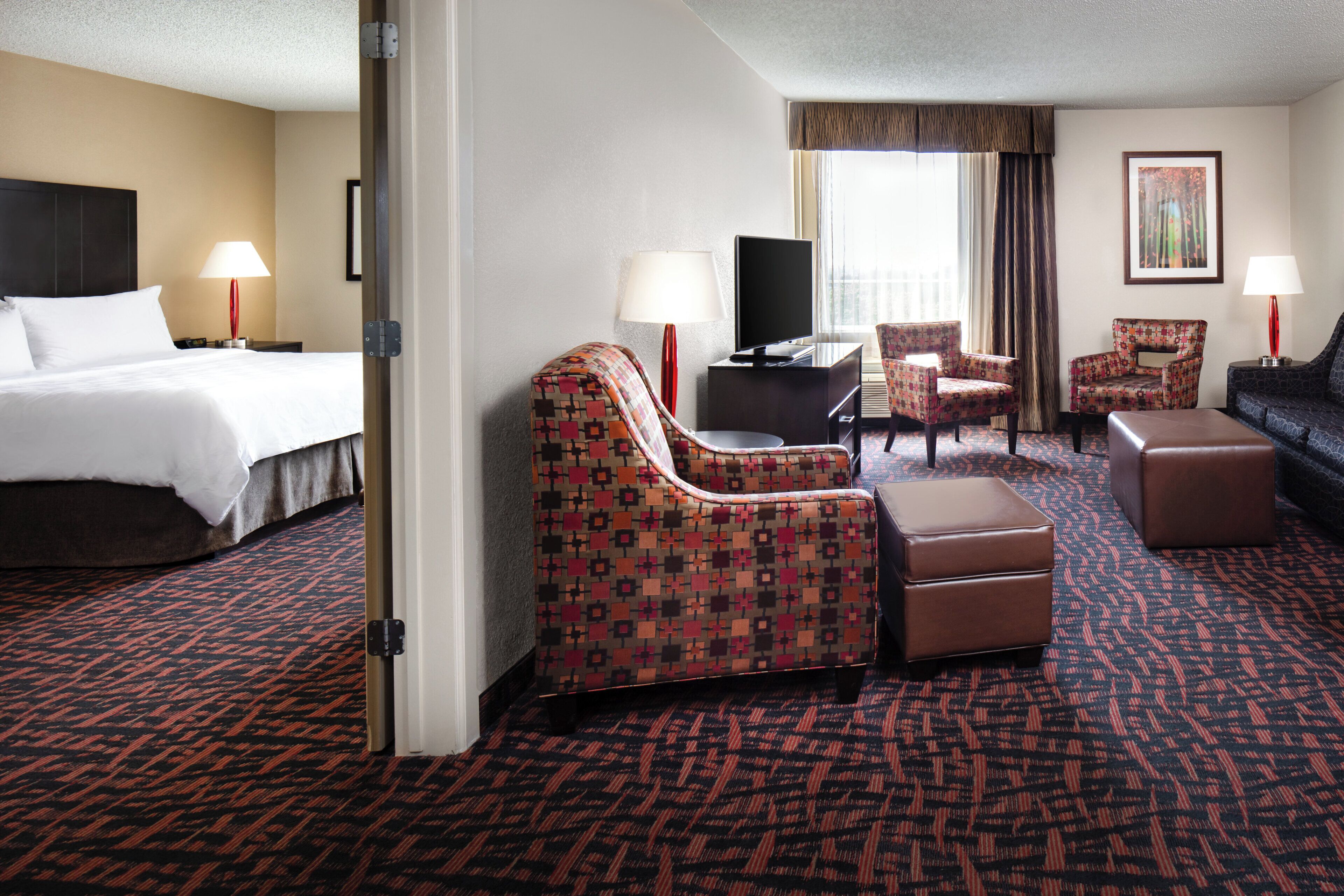 A hotel room with a bed, two armchairs, a sofa, a TV, and a desk.