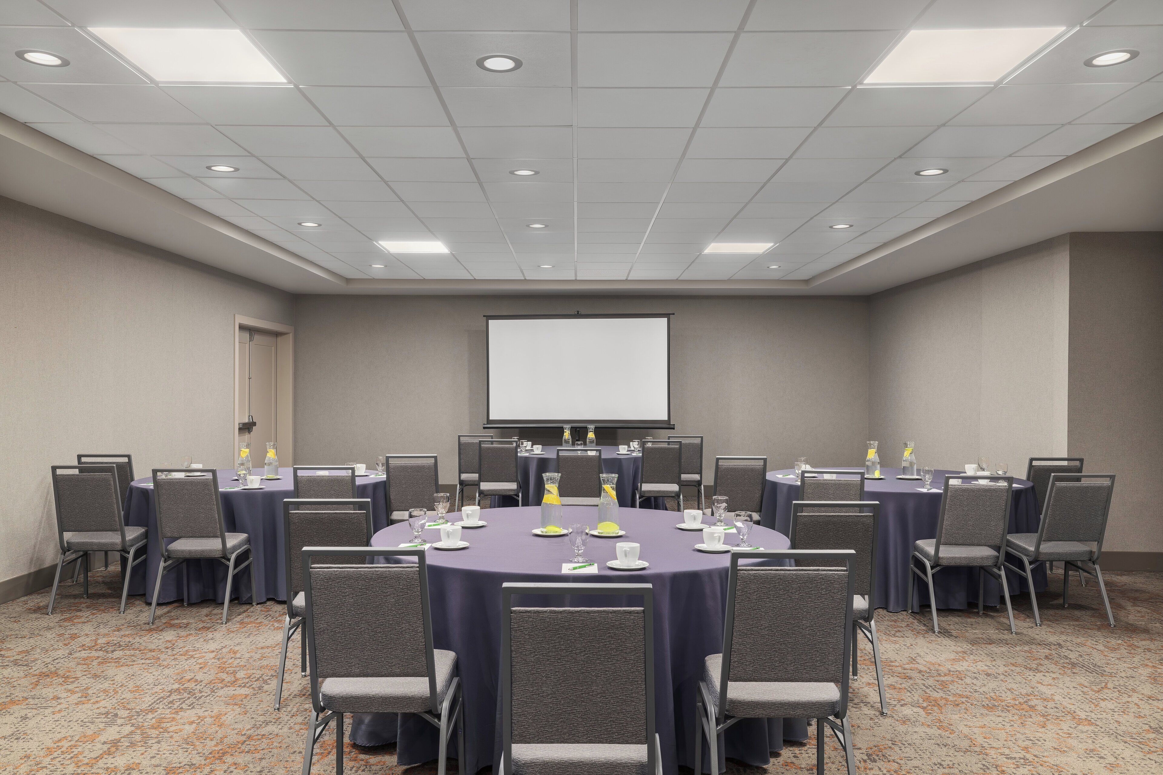 A conference room with a large table, chairs, a projector screen, and a carpeted floor.