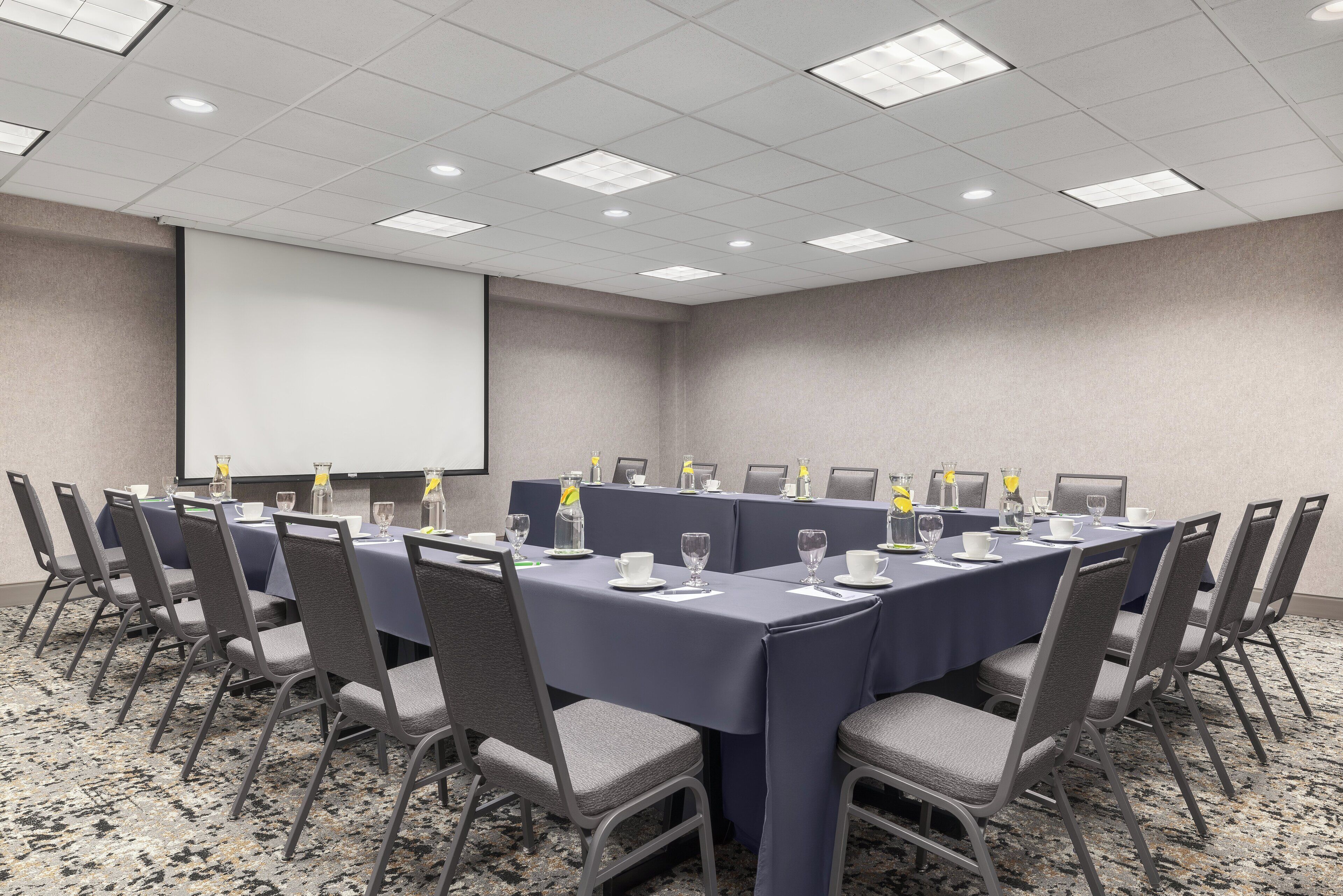 A conference room with a long table, chairs, and a projector screen.