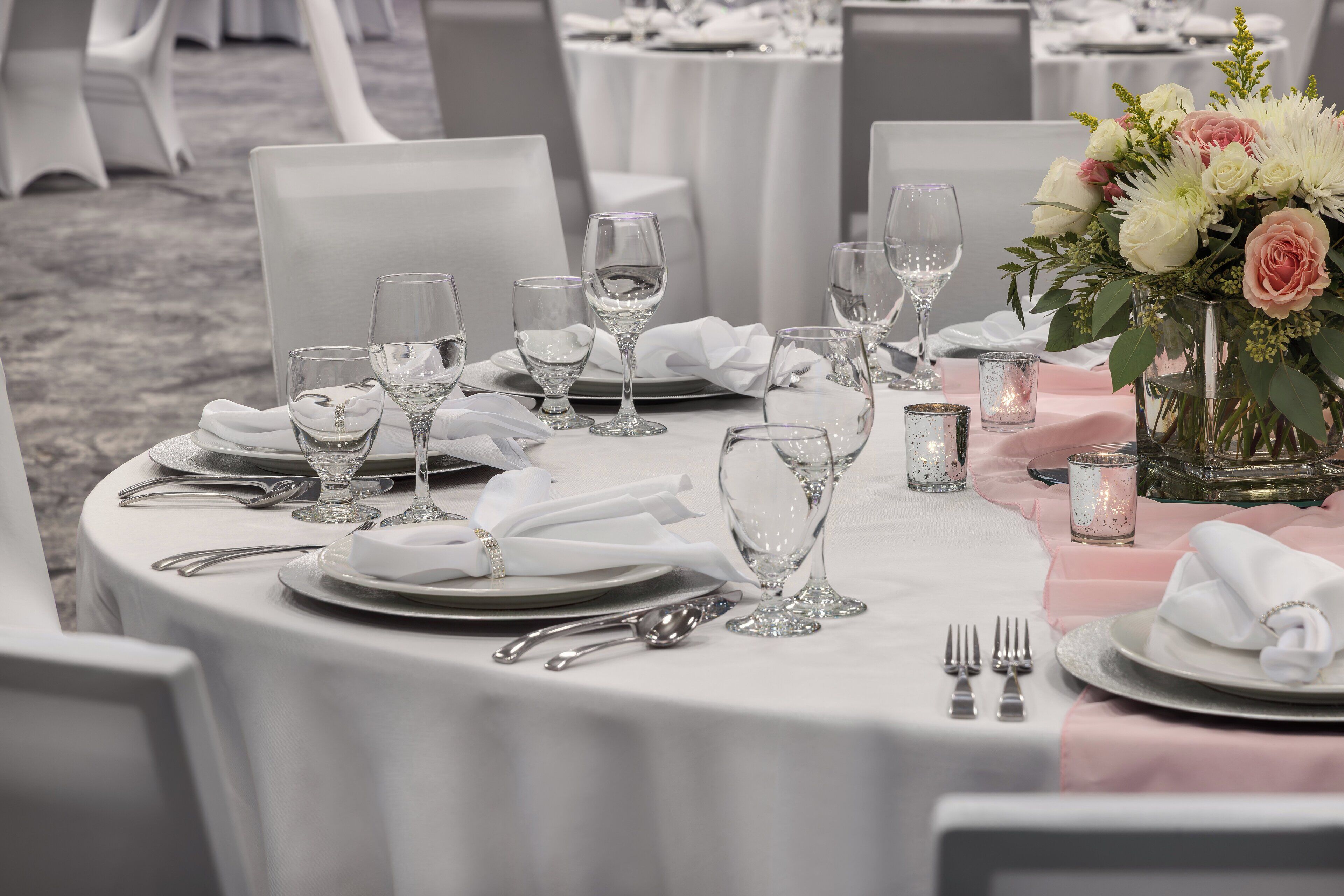 Mesa redonda para comedor dispuesta para un evento formal, con manteles blancos, cubiertos y copas de vidrio.